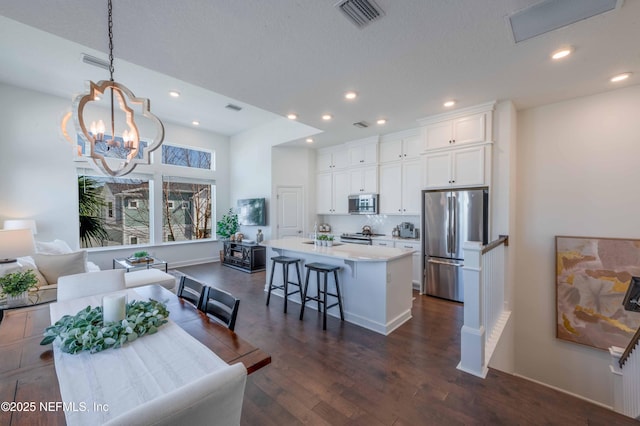 kitchen with pendant lighting, white cabinetry, stainless steel appliances, a kitchen breakfast bar, and a center island with sink