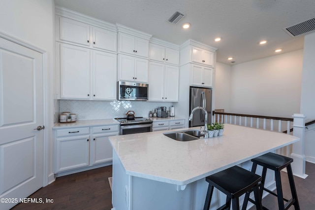 kitchen featuring white cabinetry, sink, stainless steel appliances, light stone countertops, and a center island with sink