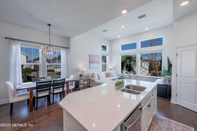 kitchen featuring stainless steel dishwasher, sink, hanging light fixtures, and a center island with sink