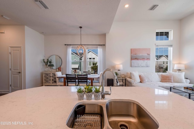 kitchen featuring sink, light stone counters, a chandelier, a textured ceiling, and pendant lighting