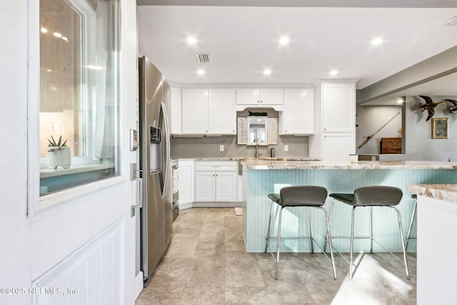 kitchen with sink, a breakfast bar area, white cabinets, stainless steel fridge with ice dispenser, and light stone countertops