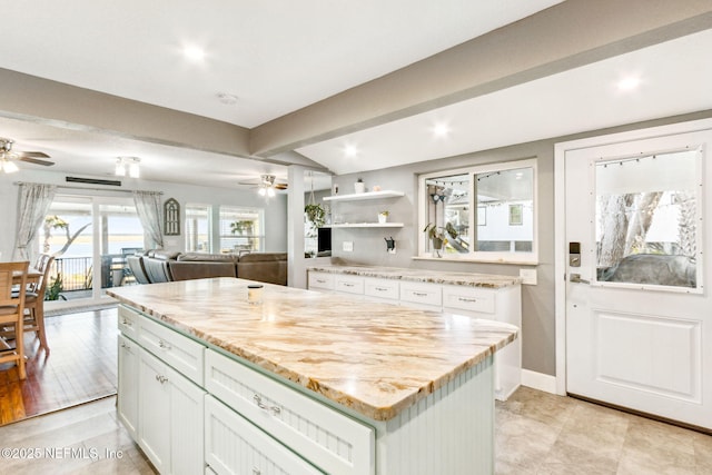 kitchen with ceiling fan, beam ceiling, light stone countertops, white cabinets, and a kitchen island