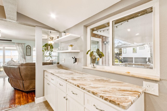 kitchen with light stone countertops, white cabinetry, lofted ceiling, and light hardwood / wood-style floors