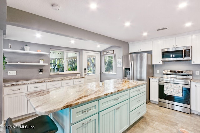 kitchen with lofted ceiling, green cabinets, white cabinetry, appliances with stainless steel finishes, and a kitchen island