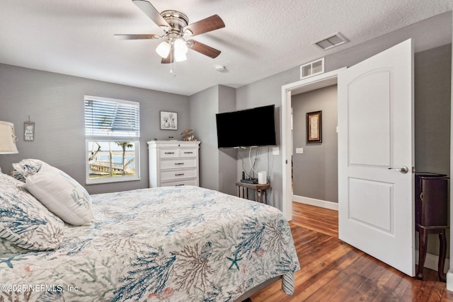 bedroom with ceiling fan, a textured ceiling, and dark hardwood / wood-style flooring