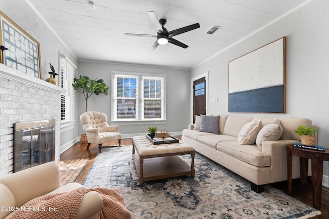 living room featuring ceiling fan, ornamental molding, a fireplace, and wood-type flooring