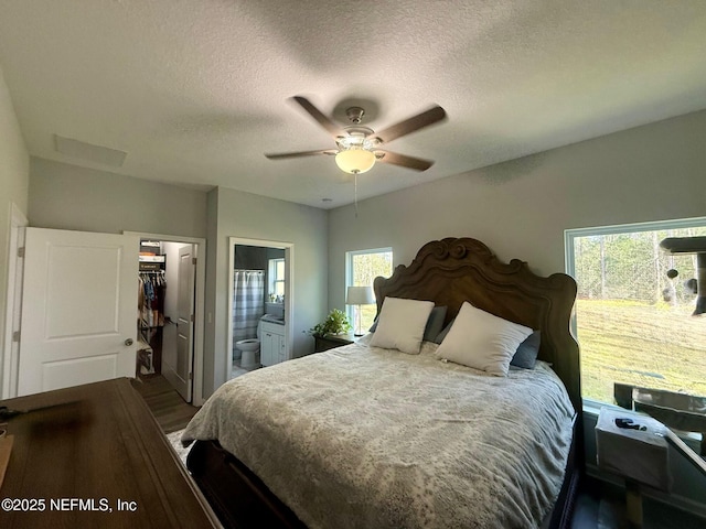 bedroom featuring a walk in closet, ensuite bathroom, ceiling fan, a textured ceiling, and wood finished floors