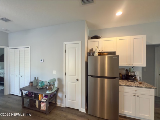 kitchen featuring stone counters, freestanding refrigerator, white cabinetry, and visible vents