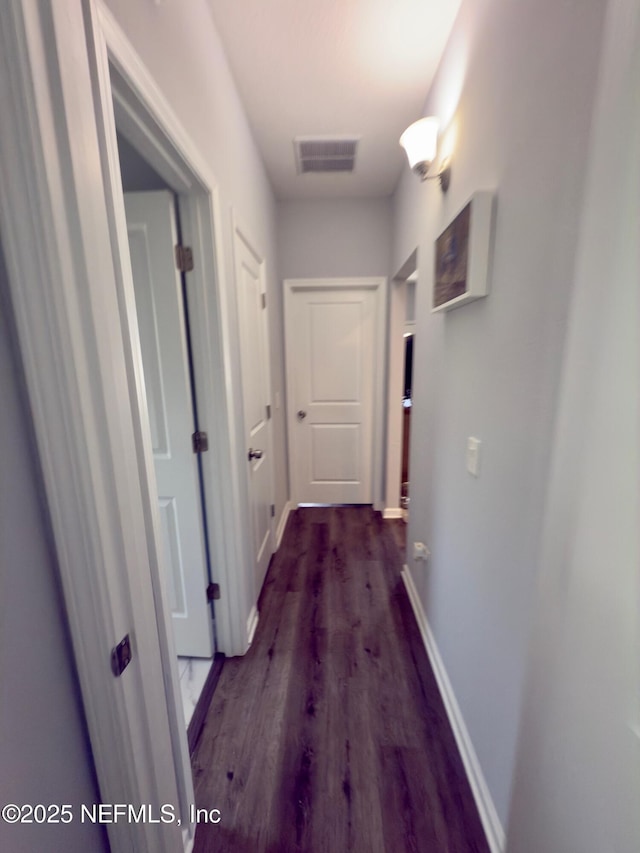 hallway featuring dark wood-type flooring, visible vents, and baseboards