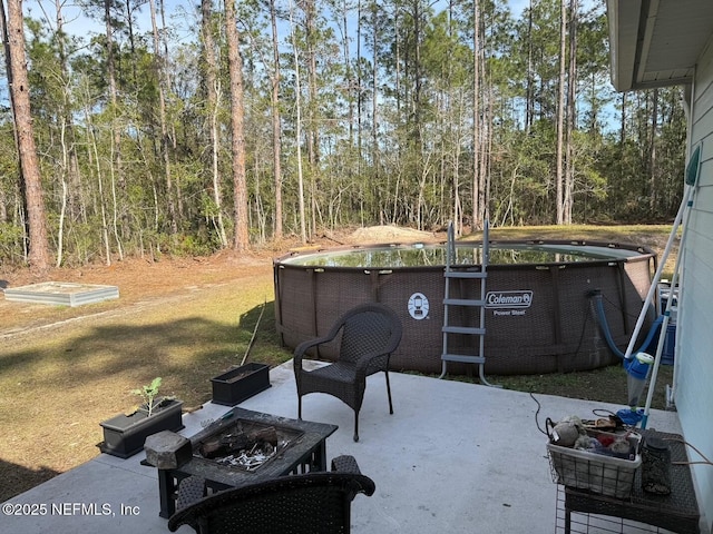 view of patio featuring a fire pit, an outdoor pool, and a view of trees