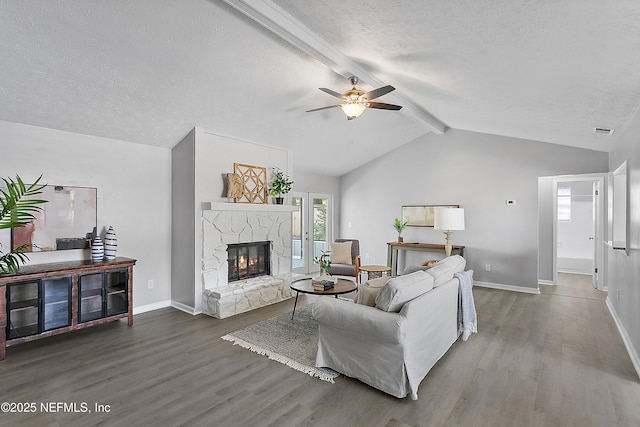 living room with vaulted ceiling with beams, a stone fireplace, dark hardwood / wood-style floors, and a textured ceiling