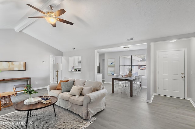 living room with ceiling fan, vaulted ceiling with beams, a textured ceiling, and light hardwood / wood-style floors