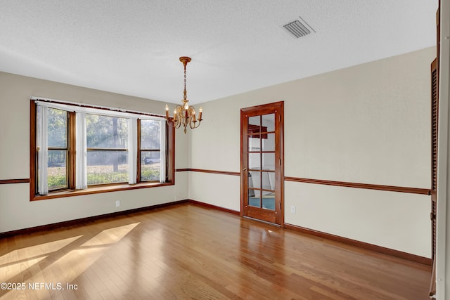 empty room with a chandelier, hardwood / wood-style floors, and a textured ceiling