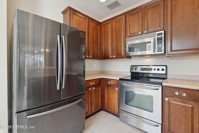 kitchen featuring stainless steel appliances, light tile patterned flooring, and a textured ceiling