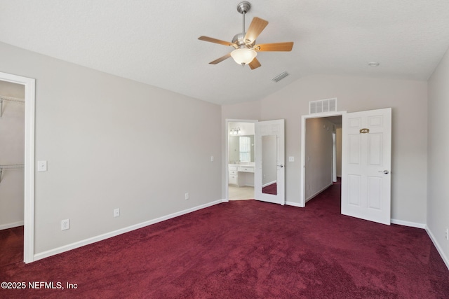 unfurnished bedroom featuring ensuite bath, vaulted ceiling, dark colored carpet, a walk in closet, and a closet