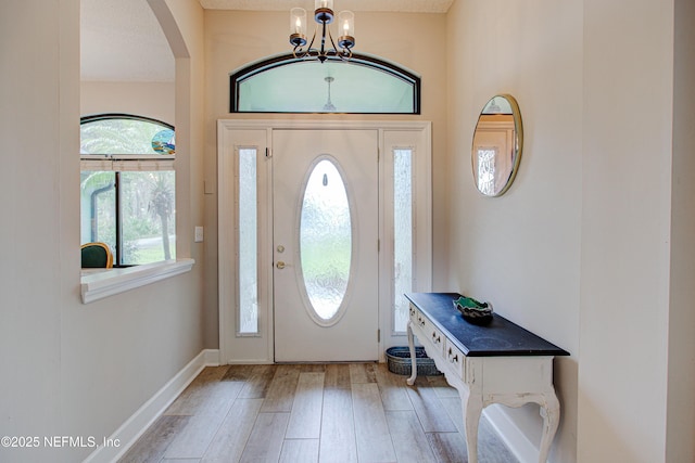 entryway featuring arched walkways, light wood-style flooring, baseboards, and an inviting chandelier