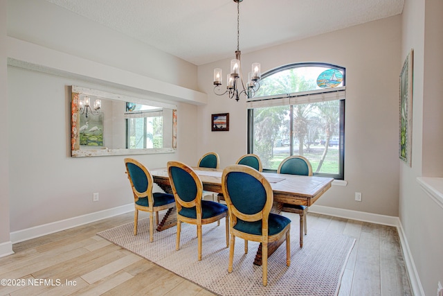 dining space with light wood-type flooring, baseboards, a chandelier, and a textured ceiling