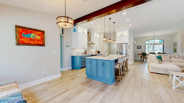 kitchen with stainless steel fridge with ice dispenser, wall chimney exhaust hood, light countertops, blue cabinetry, and a sink