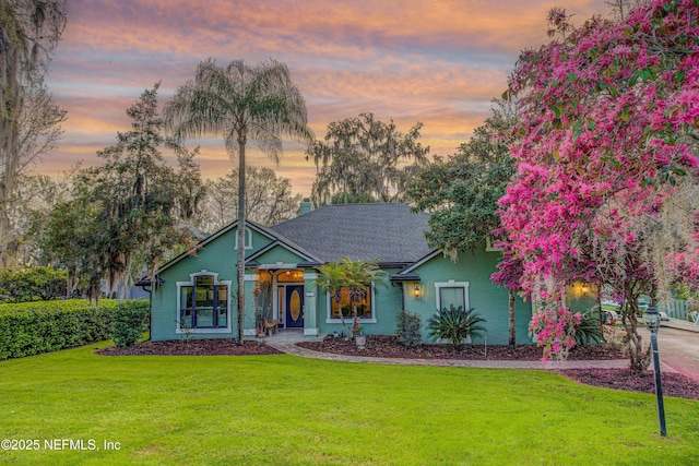 view of front of home featuring a yard, a shingled roof, and stucco siding