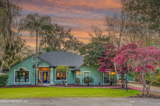 view of front of house with roof with shingles, a chimney, a front lawn, and stucco siding