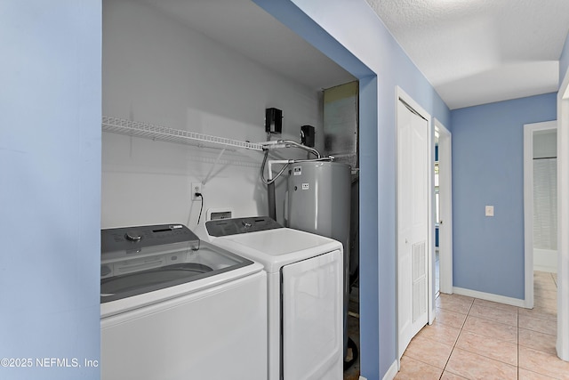 washroom with electric water heater, washing machine and dryer, a textured ceiling, and light tile patterned floors