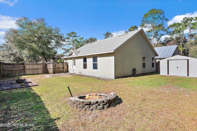 rear view of house featuring a storage shed, a lawn, and an outdoor fire pit