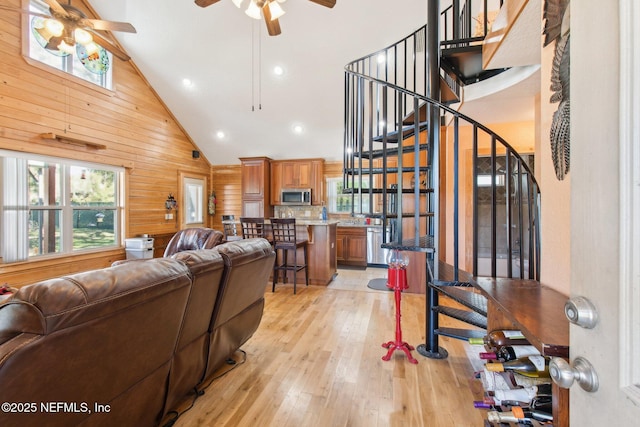 living room featuring ceiling fan, plenty of natural light, light hardwood / wood-style floors, and wood walls