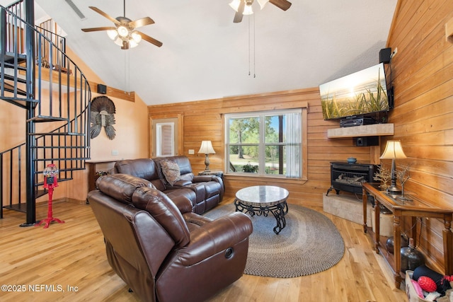 living room with wood-type flooring, wooden walls, ceiling fan, and a wood stove