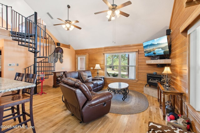 living room with hardwood / wood-style floors, high vaulted ceiling, wood walls, a wood stove, and ceiling fan