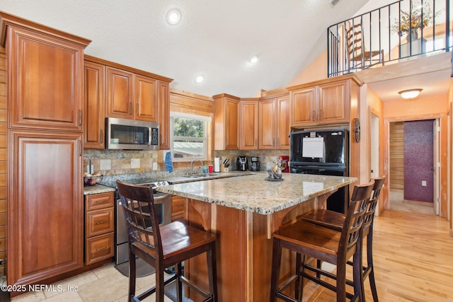 kitchen featuring light stone counters, a breakfast bar area, tasteful backsplash, and vaulted ceiling