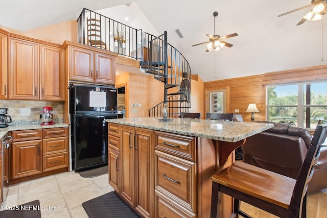 kitchen with black fridge, a kitchen breakfast bar, light stone countertops, and tasteful backsplash