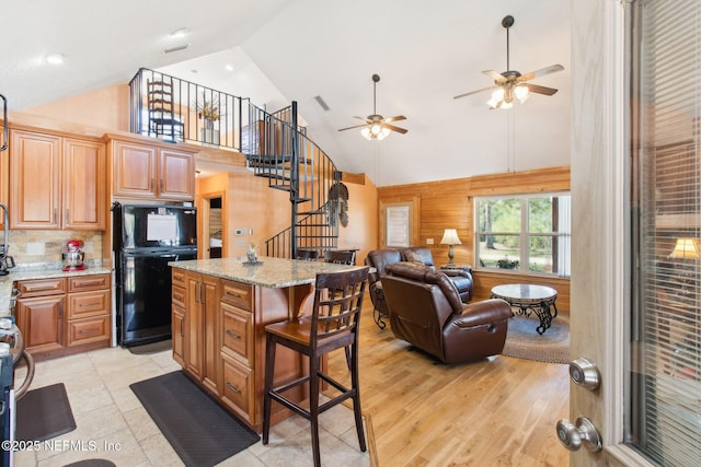 kitchen with a kitchen island, wooden walls, a kitchen breakfast bar, light hardwood / wood-style floors, and light stone countertops