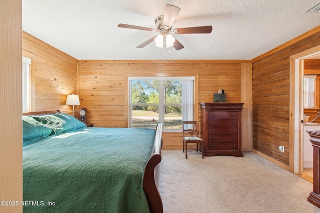 bedroom featuring ceiling fan, light carpet, a textured ceiling, and wood walls