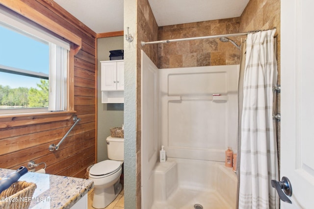 bathroom with vanity, wood walls, toilet, and walk in shower