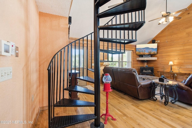 stairway featuring wooden walls, a wood stove, hardwood / wood-style floors, and high vaulted ceiling