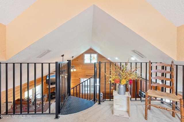 stairs featuring lofted ceiling, wooden walls, a textured ceiling, and carpet