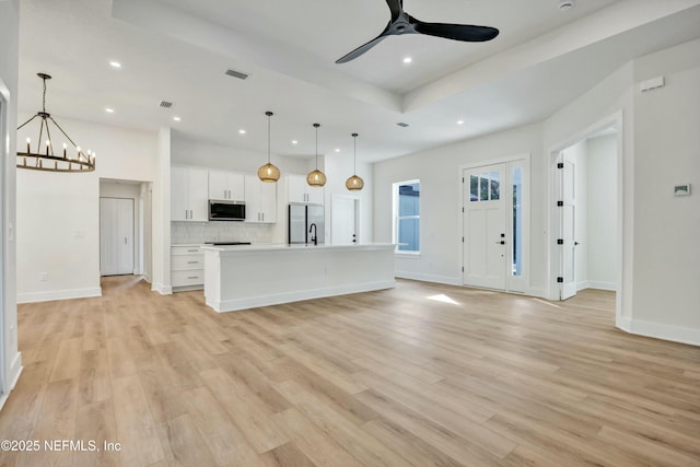 unfurnished living room featuring a raised ceiling, ceiling fan with notable chandelier, and light wood-type flooring