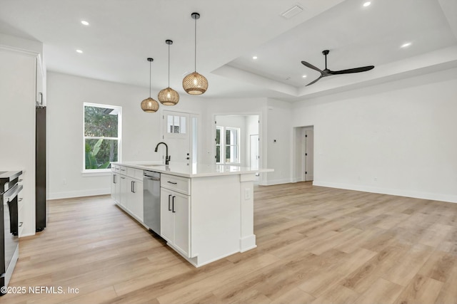 kitchen with appliances with stainless steel finishes, a kitchen island with sink, hanging light fixtures, white cabinets, and a raised ceiling