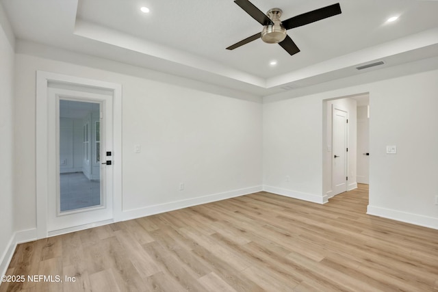 unfurnished room featuring ceiling fan, a raised ceiling, and light hardwood / wood-style flooring