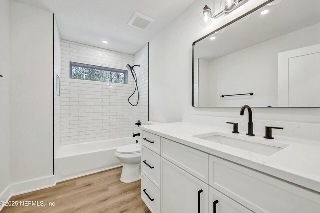 full bathroom with wood-type flooring, tiled shower / bath, vanity, and toilet