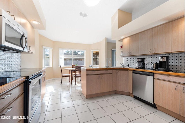 kitchen featuring tasteful backsplash, stainless steel appliances, light brown cabinetry, and light tile patterned floors