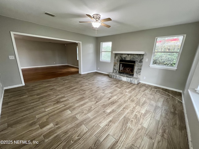 unfurnished living room featuring a stone fireplace, wood-type flooring, and ceiling fan