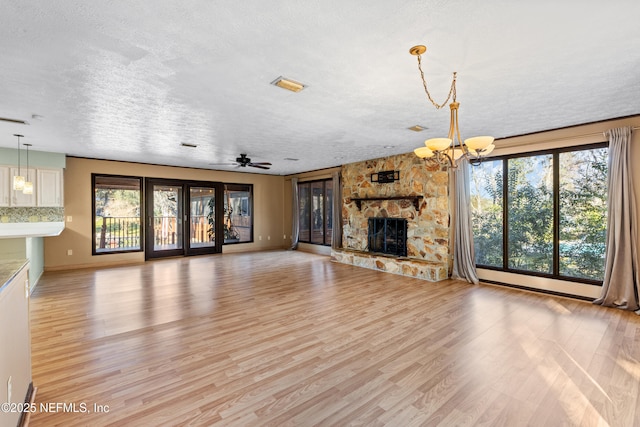 unfurnished living room with a stone fireplace, a textured ceiling, and light hardwood / wood-style flooring