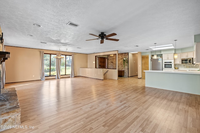 unfurnished living room with ceiling fan, sink, a textured ceiling, and light hardwood / wood-style floors