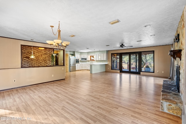 unfurnished living room with ceiling fan with notable chandelier, a fireplace, light hardwood / wood-style floors, and a textured ceiling