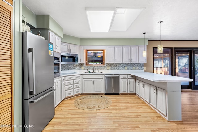 kitchen with pendant lighting, sink, a skylight, stainless steel appliances, and kitchen peninsula