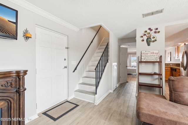 entryway with ornamental molding, light hardwood / wood-style floors, and a textured ceiling