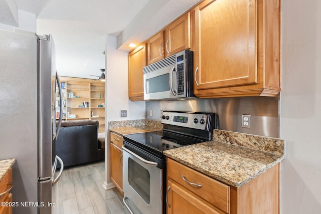 kitchen with light stone counters, ceiling fan, and stainless steel appliances