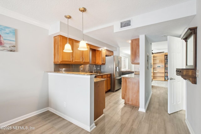 kitchen featuring hanging light fixtures, stainless steel refrigerator with ice dispenser, light stone countertops, a textured ceiling, and kitchen peninsula