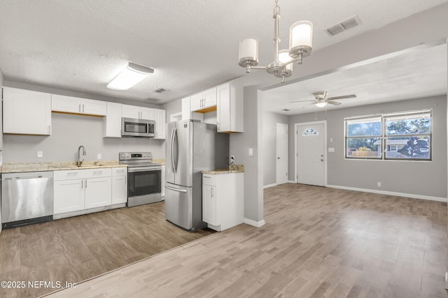 kitchen with decorative light fixtures, white cabinetry, hardwood / wood-style flooring, stainless steel appliances, and a textured ceiling